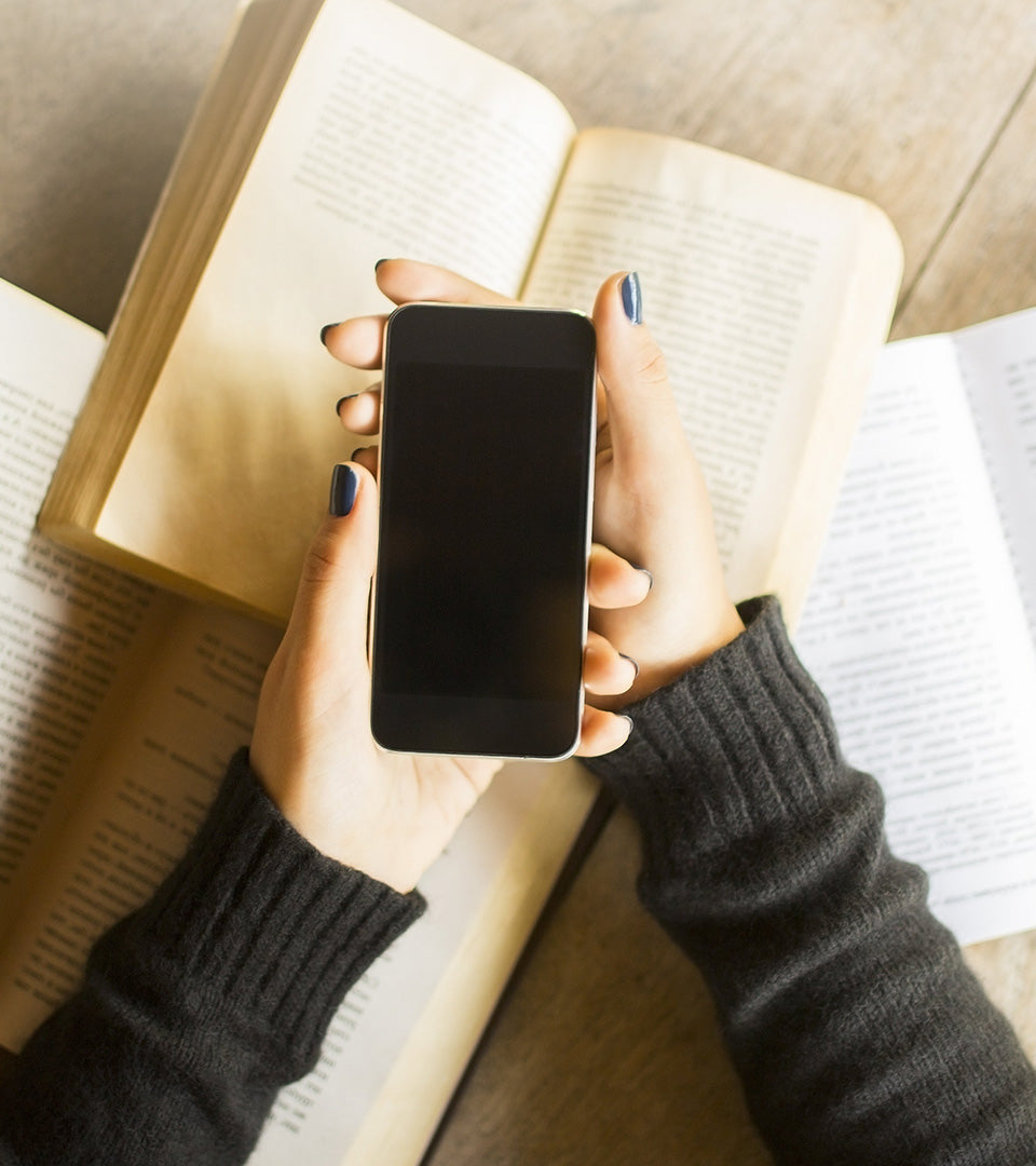 female Caucasian hands holding smartphone with open books underneath