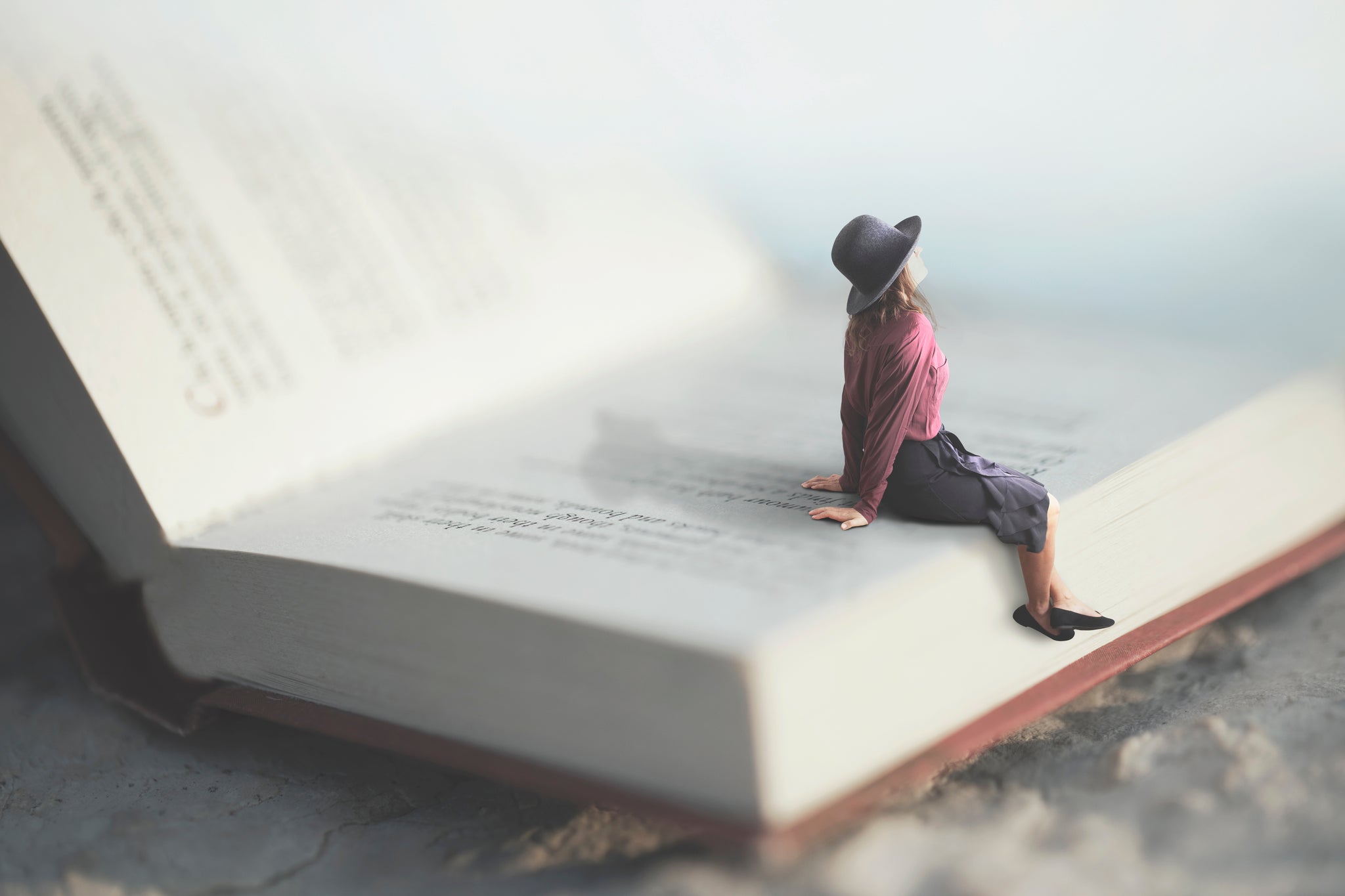 miniature woman sitting on an open book looking up 